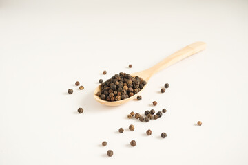 Black peppercorns poured on wooden spoon