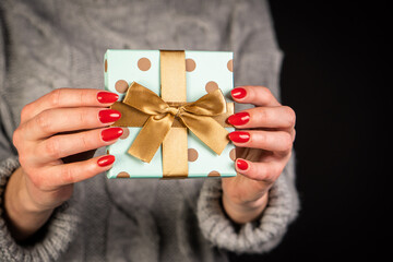 Close up shot of female hands holding a small christmas gift wrapped with ribbon.