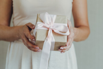 Close-up of female hands holding a small gift wrapped with a satin ribbon