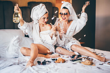Fototapeta na wymiar Woman wearing bathrobe sitting on bed and throwing confetti, young women celebrating wedding or birthday, 