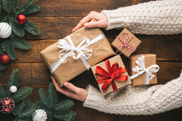 Female hands hold Christmas presents on a wooden table background. Concept of Christmas, New Year winter holidays. Homemade presents craft packages