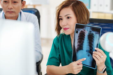 Smiling female surgeon video calling coworker and showing chest x-ray to get advice on tumor