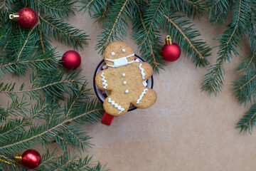 Christmas composition. Gingerbread man in a medical mask on a wooden background with red balls and a green Christmas tree.