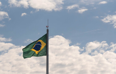 Brazilian flag flying and in the background the blue sky with white clouds