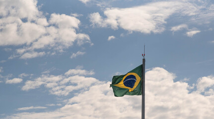 Brazilian flag flying and in the background the blue sky with white clouds
