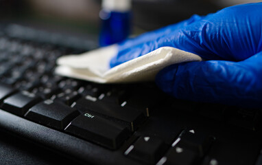Hand in protective glove with napkin cleaning keyboard. Covid-19 disinfection concept.