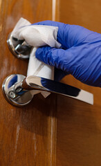Hand in protective glove with napkin cleaning door handle. Covid-19 disinfection concept.