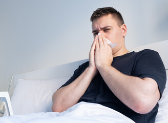 A man with a cold blows his nose in bed. The man fell ill. Influenza, allergies, coronavirus