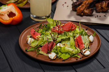 Caesar salad with grapefruit with grilled pork ribs, pickled vegetables and moonshine  on black wooden background