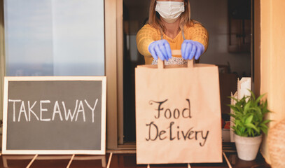 Woman at work holding food delivery paper bag while wearing surgical gloves and face mask for coronavirus - Concept of safety measures at work and takeaway