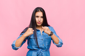 young woman looking confident, angry, strong and aggressive, with fists ready to fight in boxing...