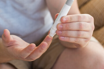 Medicine, diabetes, glycemia, healthcare and people concept - close up of a man's hands using a lancet on his finger to check blood glucose meter with copy space for text