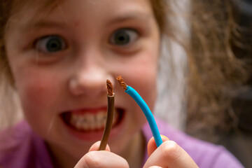 A little girl plays dangerously with electricity. The child is trying to connect two live copper...