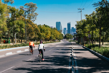 a couple riding a bicycle with protective equipment and in the background is the city on a sunny day