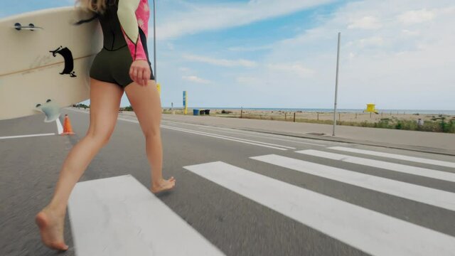 Beautiful and attractive young woman walk to beach in short wetsuit. Run across the street in California town. Millennial generation z teenager do active extreme sports as hobby