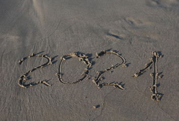 Abstract background photo of coming New Year 2021 on the beach. Handwritten inscription 2021 on the...