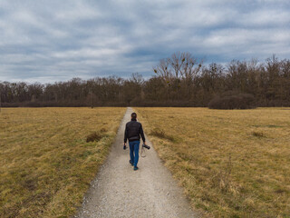 Man walk on Long path to forest between yellow fields at sunny morning