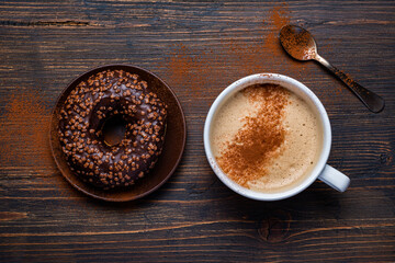 on the rustic wooden background, delicious breakfast with cappuccino and chocolate glazed donuts
