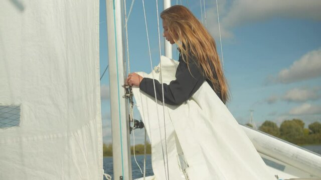 A beautiful young sportswoman studies the rigging and rigging of a sports yacht. Learning to raise a sail.