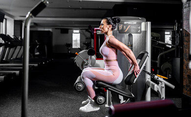 Fototapeta na wymiar A girl in sportswear in a professional gym works out with fitness equipment. Healthy lifestyle concept