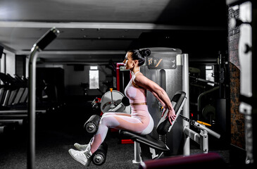 Fototapeta na wymiar A girl in sportswear in a professional gym works out with fitness equipment. Healthy lifestyle concept