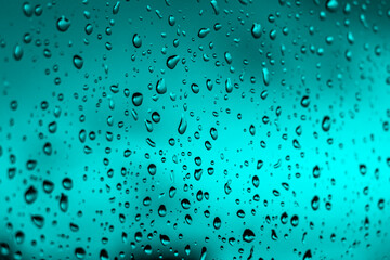 Bright fiery sunset through raindrops on window with bokeh lights. Abstract background. Water drop on the glass against the blurred silhouettes high-rise city.