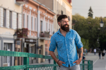 Half length portrait of bearded hipster man dressed in stylish shirt while standing in the street, glamorous male with cool fashion style, outdoors.