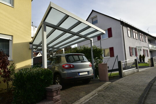 Neuer grauer Carport aus beschichtetem Aluminium mit Pult-Glasdach an einem Wohnhaus