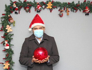 latin man with protection mask, santa claus hat and red sphere,
Christmas decoration, new normal...