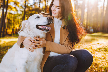 Young woman walk and play with her golden retriever in yellow autumn park. Friendship, care, pet love concept.