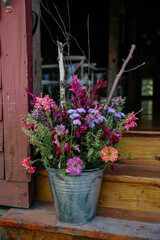 Fototapeta na wymiar metal bucket of pink and purple flowers on steps of farmhouse