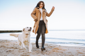 Young woman walk with her pet golden retriever by seaside at autumn sunny day