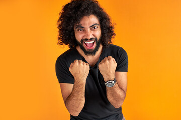 happy young indian or arab man celebrating surprised and amazed by win, winner concept. cheerful guy with long dark hair shine with happiness