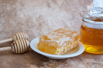 glass jar full of honey, plate with honeycomb on light brown background