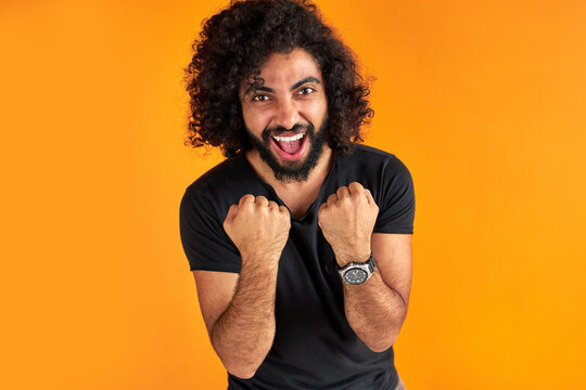 happy young indian or arab man celebrating surprised and amazed by win, winner concept. cheerful guy with long dark hair shine with happiness