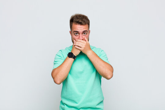 young man covering mouth with hands with a shocked, surprised expression, keeping a secret or saying oops
