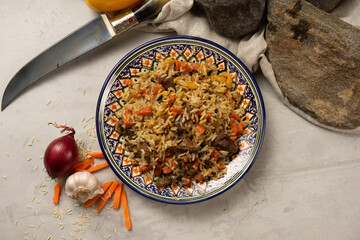 Hot pilaf with lamb or beef in a decorative national Uzbek plate with a traditional pattern. A classic oriental dish made of boiled rice, meat and vegetables with spicy spices.