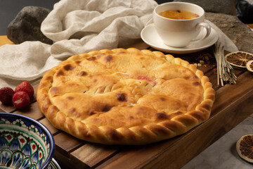 Hot Ossetian sweet pie with strawberry filling next to decorative national Uzbek ceramic dishes with a traditional pattern. Classic oriental pastries for dessert for tea.