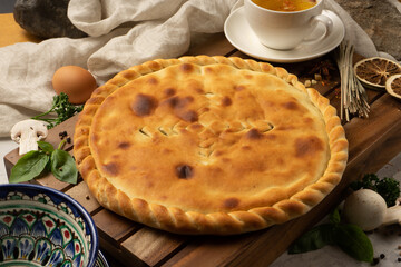 Hot Ossetian pie with mushroom filling and herbs next to decorative national Uzbek ceramic dishes with a traditional pattern. Classic oriental pastries for tea.