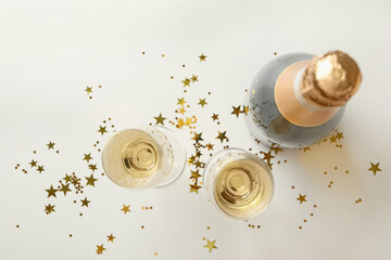 Bottle and glasses of champagne and glitter on white background