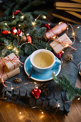 Obraz na płótnie Canvas Delicious freshly brewed thyme tea in a blue cup standing on the warm cozy piled cover with red christmas ornamental hearts, little wrapped gifts, fireflies, pine cones on the wooden table background 