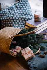 Fresh spruce in a wicker basket with wrapped gifts and pile of books on the background, indoor cozy view
