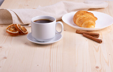 a white ceramic cup with black espresso, french croissant as breakfast or snack concept on rustic, natural texture wooden surface
