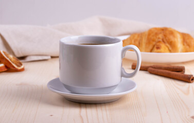 a white ceramic cup with black espresso, french croissant as breakfast or snack concept on rustic, natural texture wooden surface