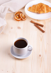 a white ceramic cup with black espresso, french croissant as breakfast or snack concept on rustic, natural texture wooden surface