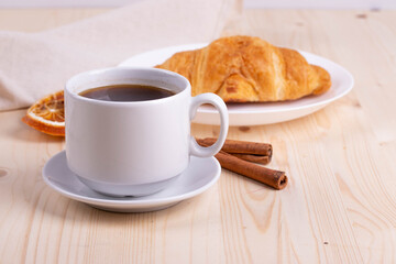 a white ceramic cup with black espresso, french croissant as breakfast or snack concept on rustic, natural texture wooden surface