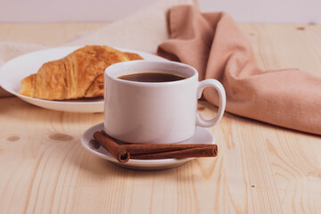 a white ceramic cup with black espresso, french croissant as breakfast or snack concept on rustic, natural texture wooden surface