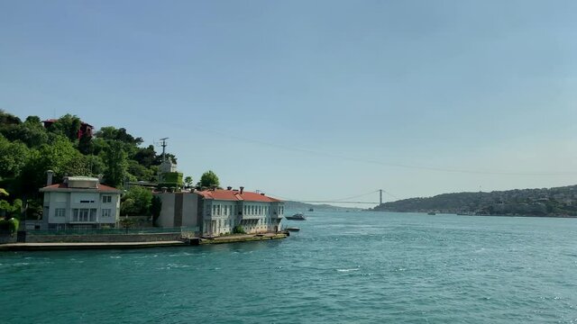 Footage of a yacht passing on Bosphorus by upscale neighborhood called "Kandilli" in Istanbul. It is a beautiful scene in a sunny summer day. Camera moves forward.