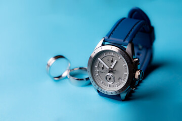 Reloj de pulsera plateado con correa azul sobre fondo azul cielo y anillos desenfocados con espacio para texto. Accesorios para hombre.