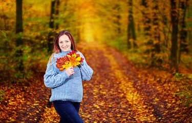 Girl with leaves in her hands in the autumn forest posing for the camera.